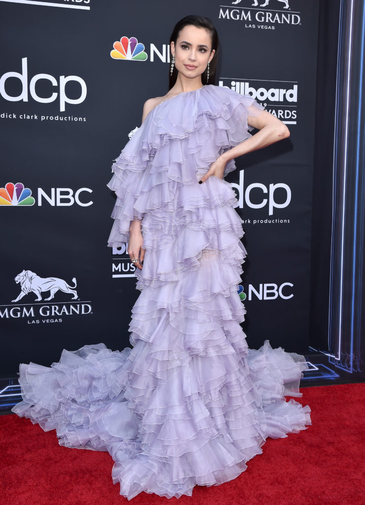 Sofia Carson poses on red carpet wearing lilac one shouldered, ruffle gown at 2019 BBMAs